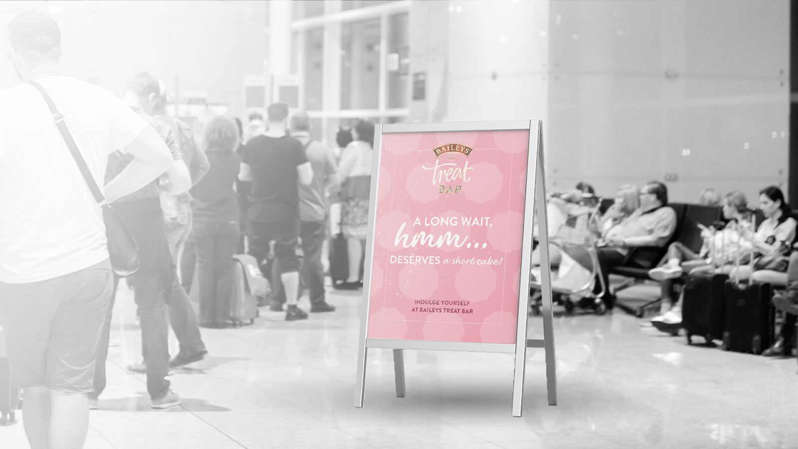A pink Baileys Treat Bar A-frame sign in an airport queue: 'A long wait, hmm... deserves a short cake!'